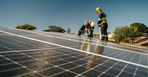 Two workers installing solar panel on roof